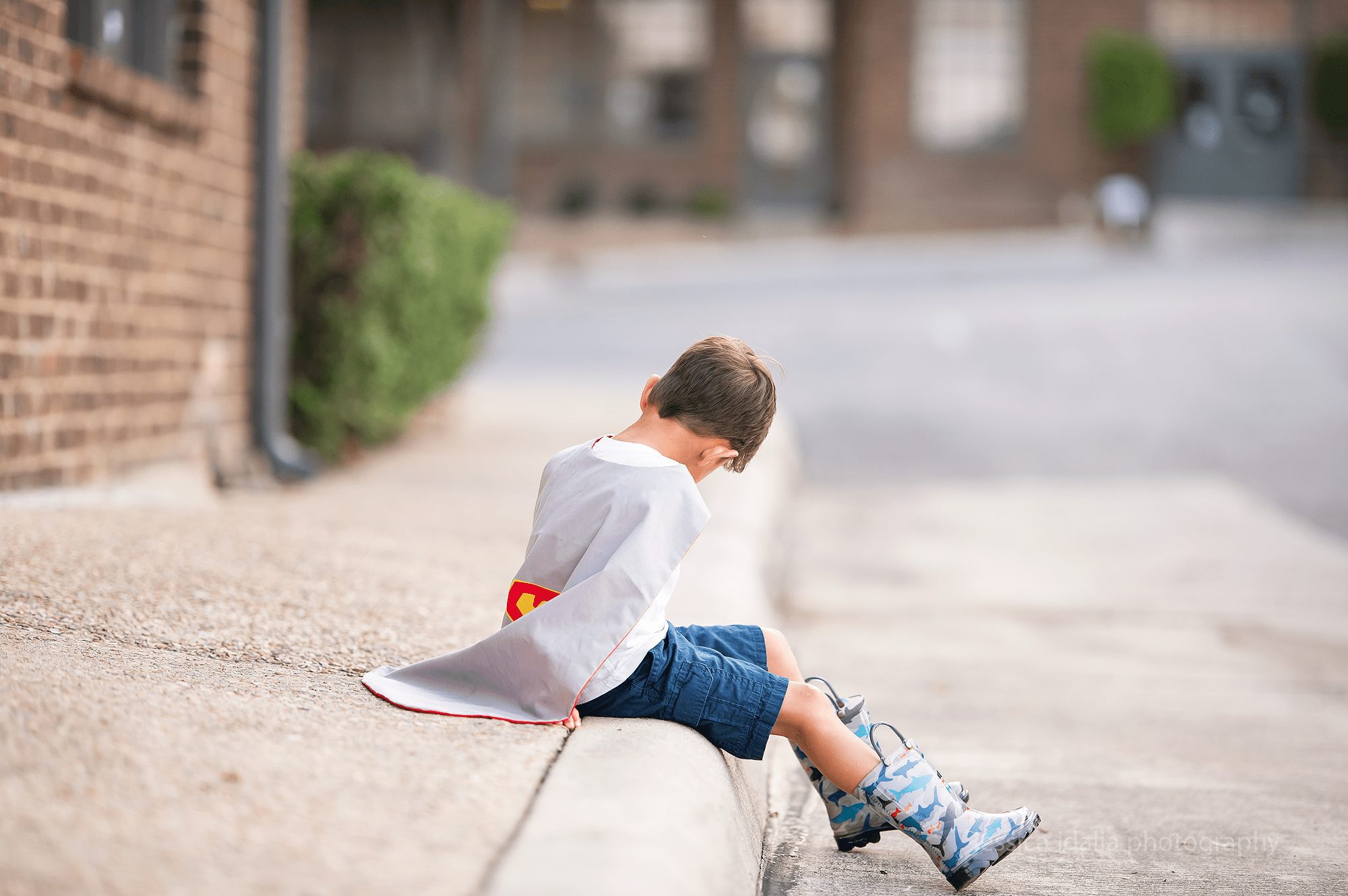 Boy with cape sitting on curb